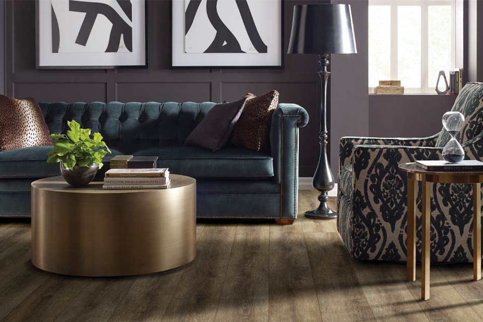 luxury vinyl flooring in living room with green velvet couch and patterned chair with mixed metal decor.